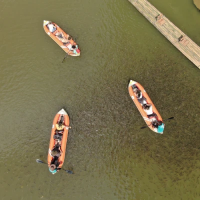 Aerial view of four wooden boats with people wearing life jackets on greenish water near a wooden dock.
